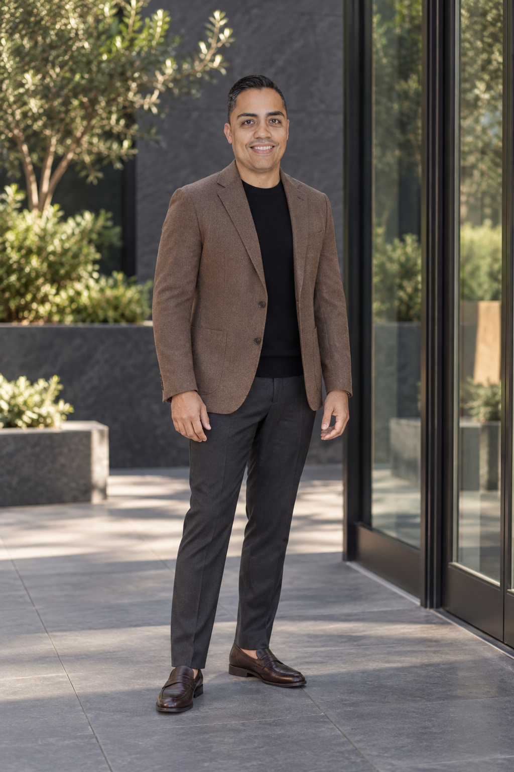 Eric wearing a brown blazer beside glass courtyard doors