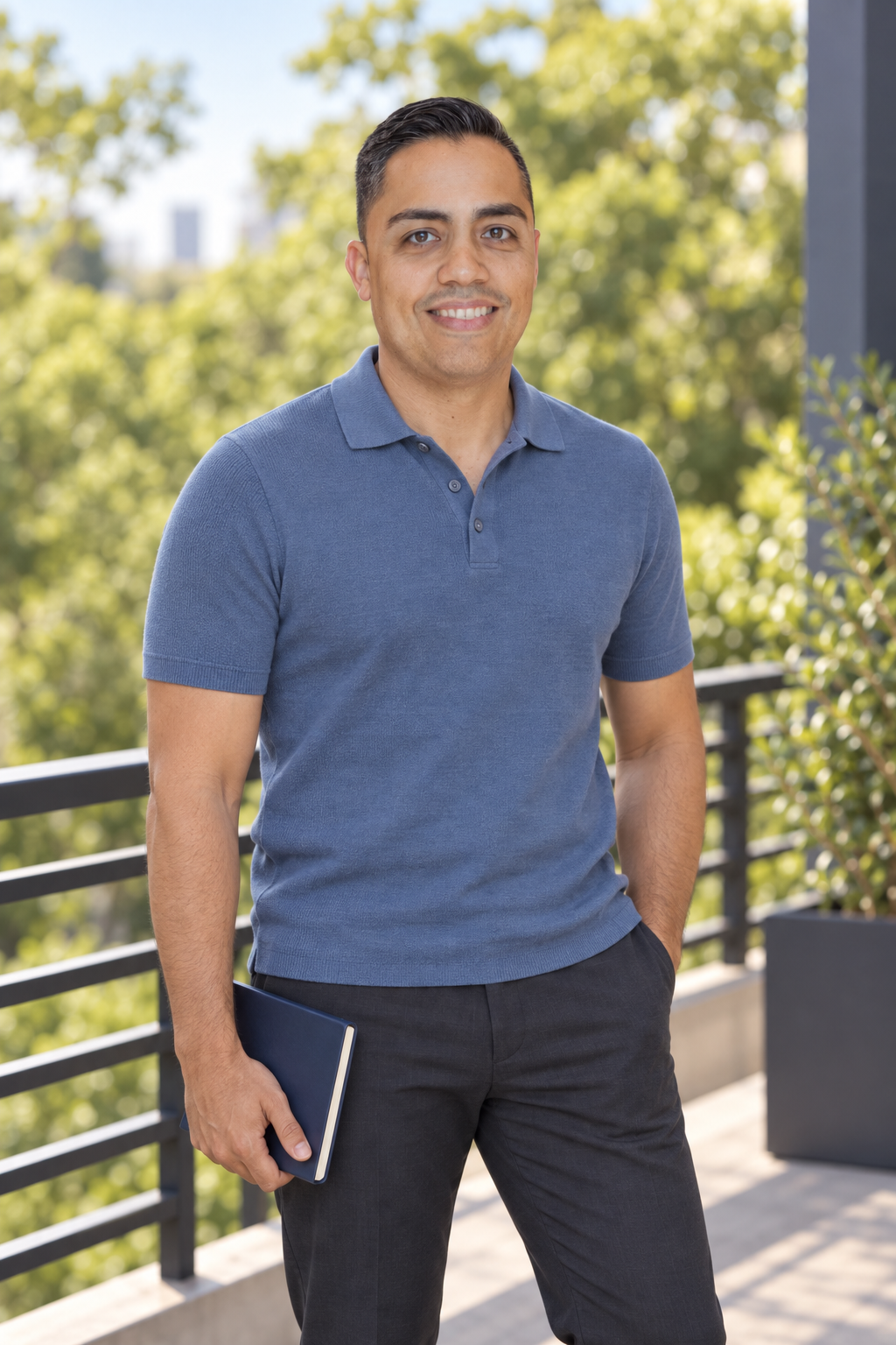 Eric in a blue polo holding a notebook on a terrace